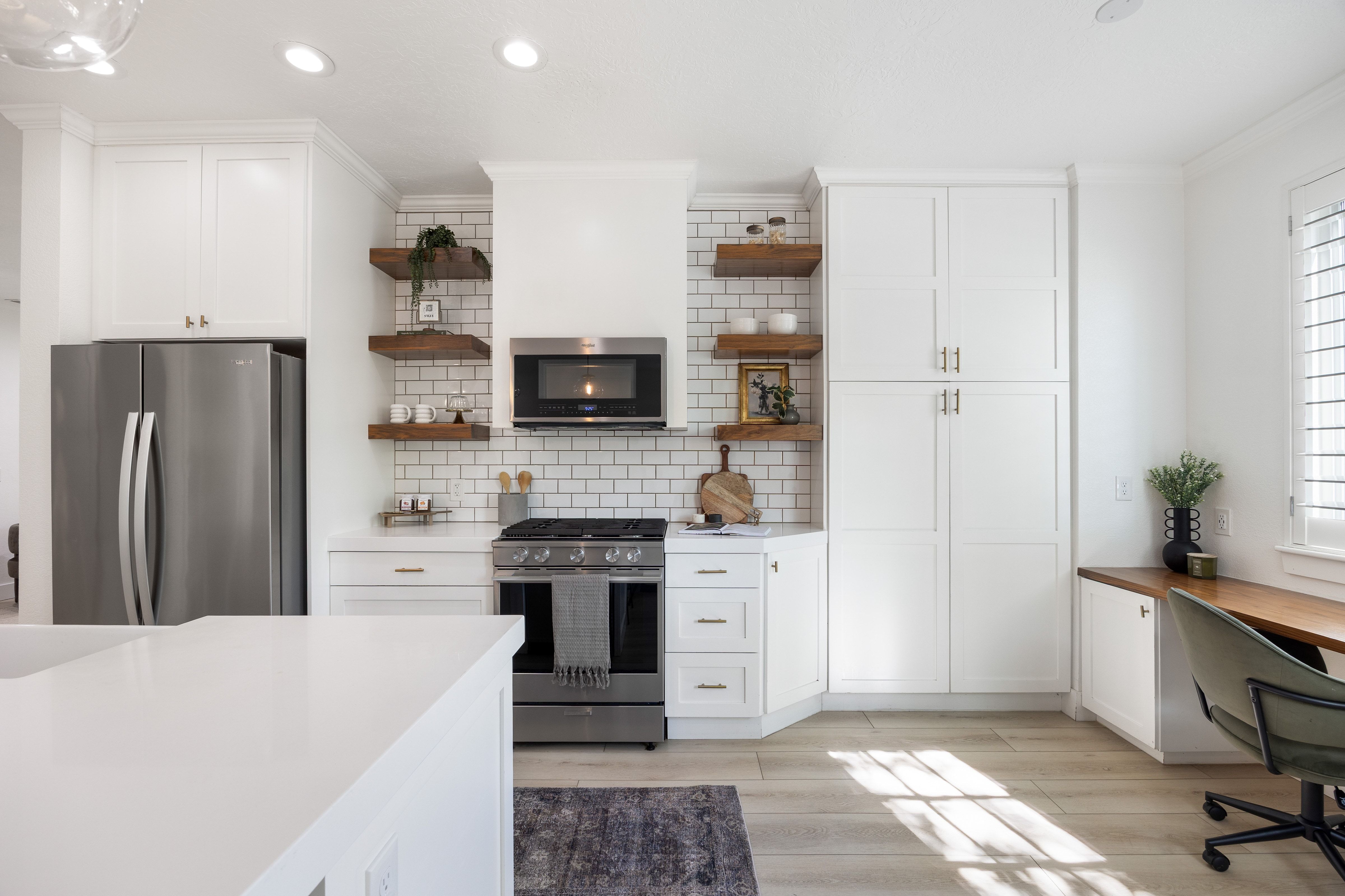 Well-appointed kitchen featuring white cabinetry, stainless steel appliances, open shelving, subway tile backsplash, and wood-finish flooring
