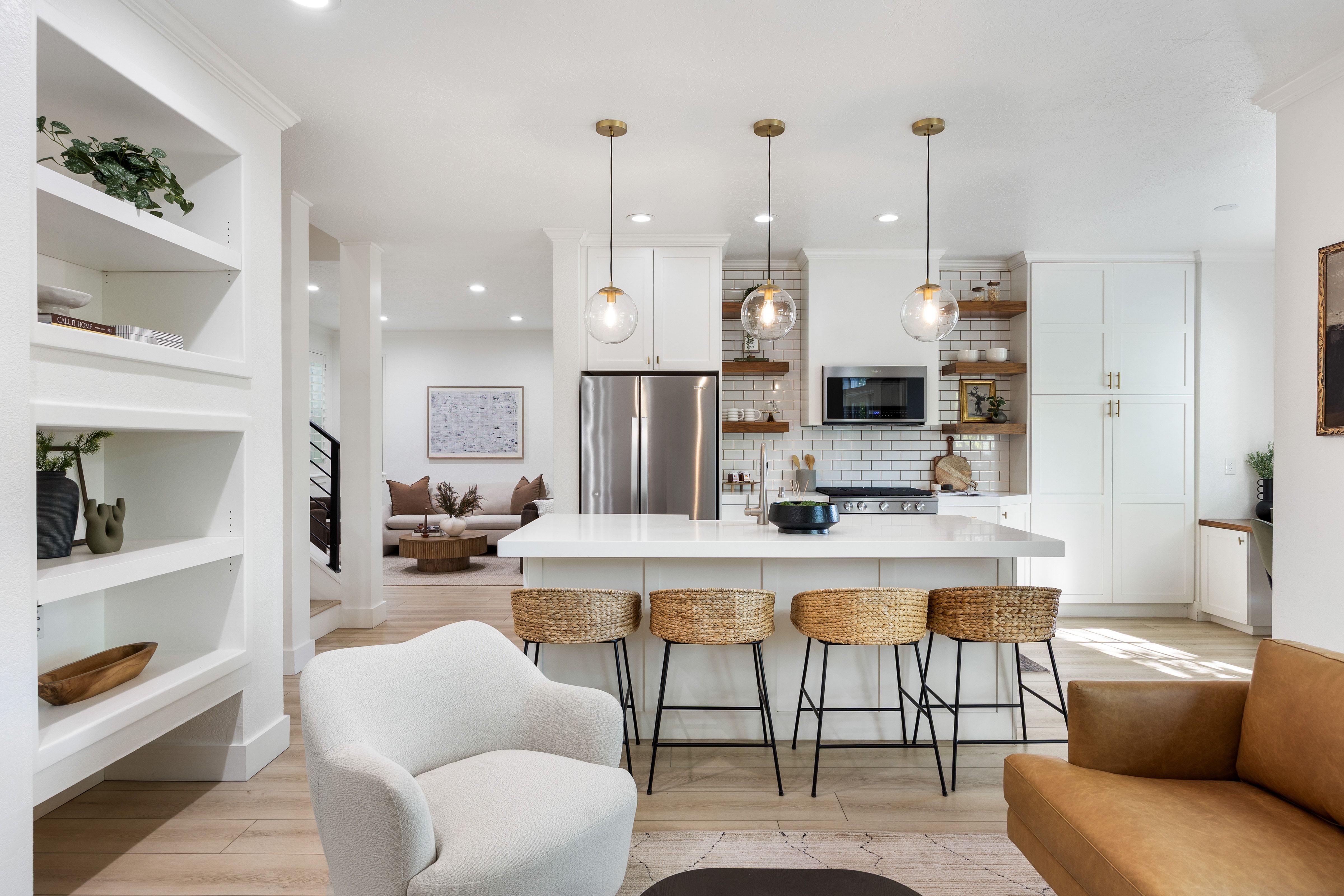 Contemporary kitchen featuring a large island with white countertop, subway tile backsplash, stainless steel appliances, and open wood shelving