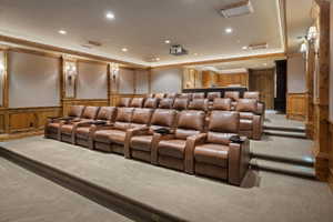 Dedicated home theater featuring tiered seating, built-in projector, recessed lighting, wood-paneled walls, and integrated sconces