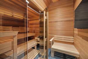 Private sauna featuring clear glass door, multiple slatted wood benches, slatted wood walls and ceiling, and dark tile flooring