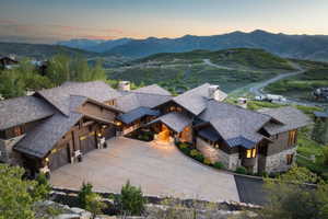 Expansive property featuring a stone and wood facade, multiple gabled roofs, an attached multi-car garage, a paved driveway, and mature landscaping, all set against a mountainous backdrop