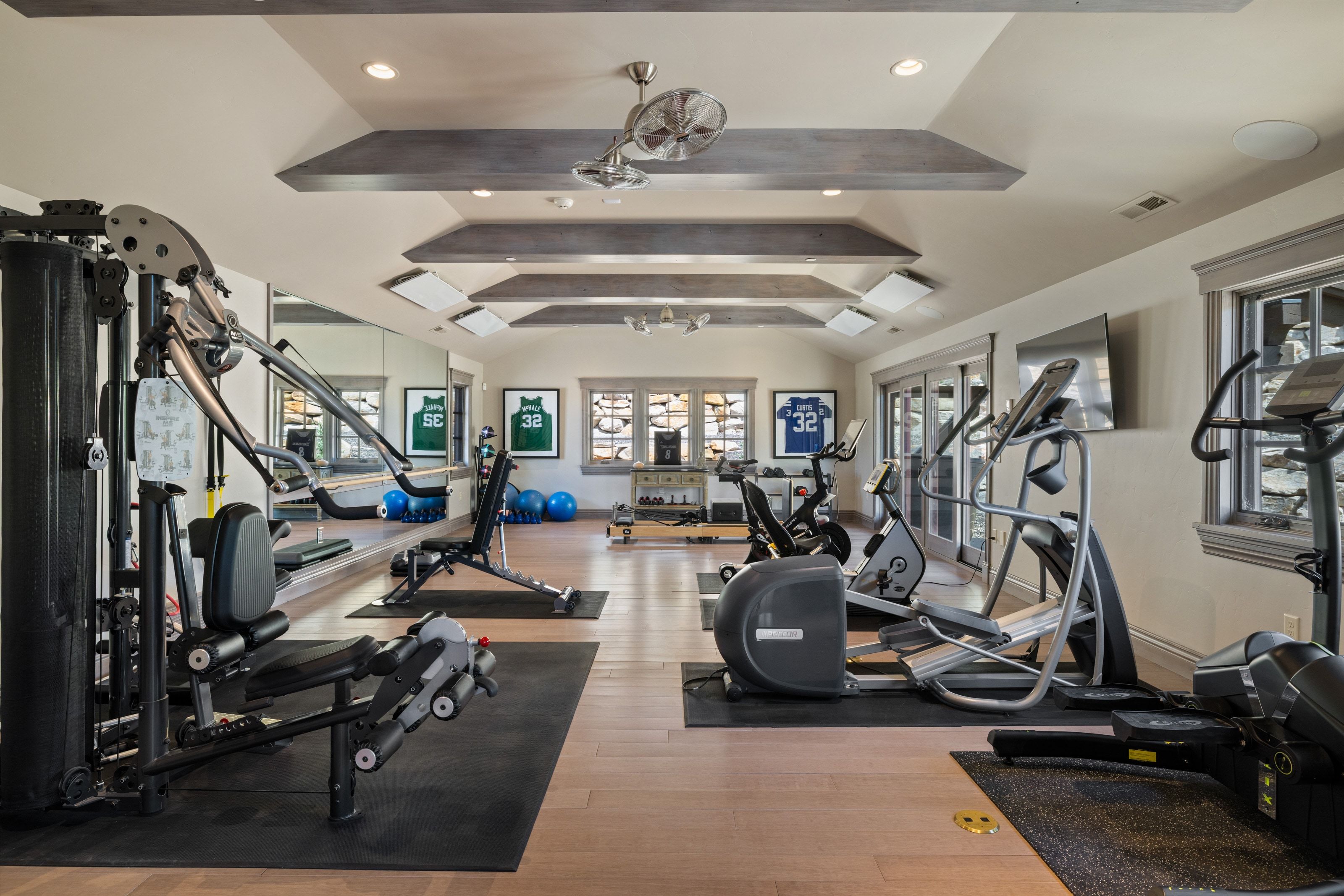 Dedicated fitness space featuring wood-finish flooring, recessed lighting, and tray ceilings with exposed wood beams