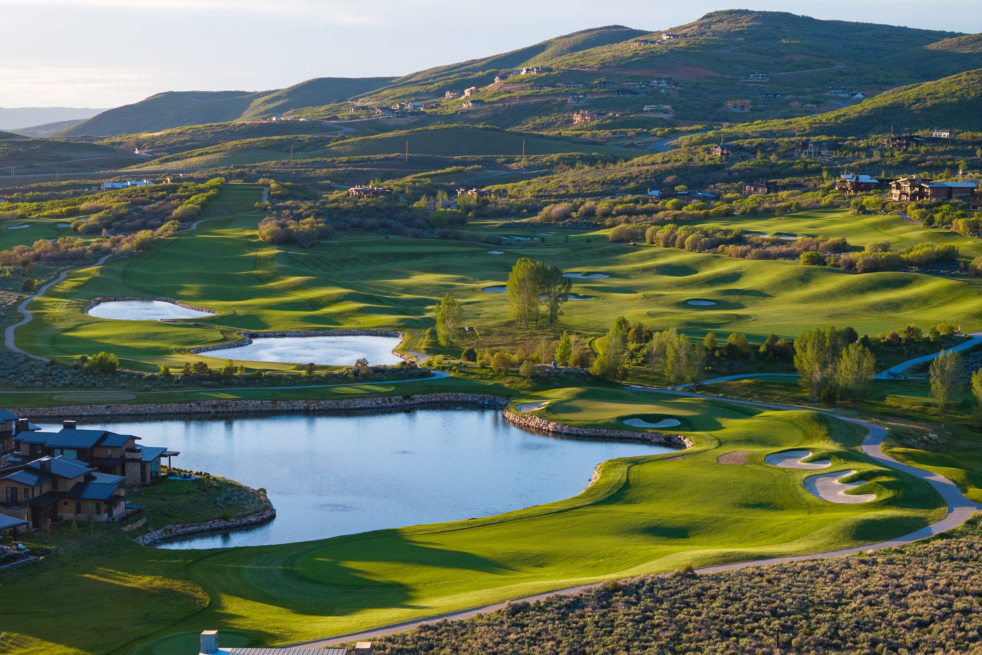 Expansive golf course setting featuring manicured greens, multiple water features, sand traps, and golf cart paths