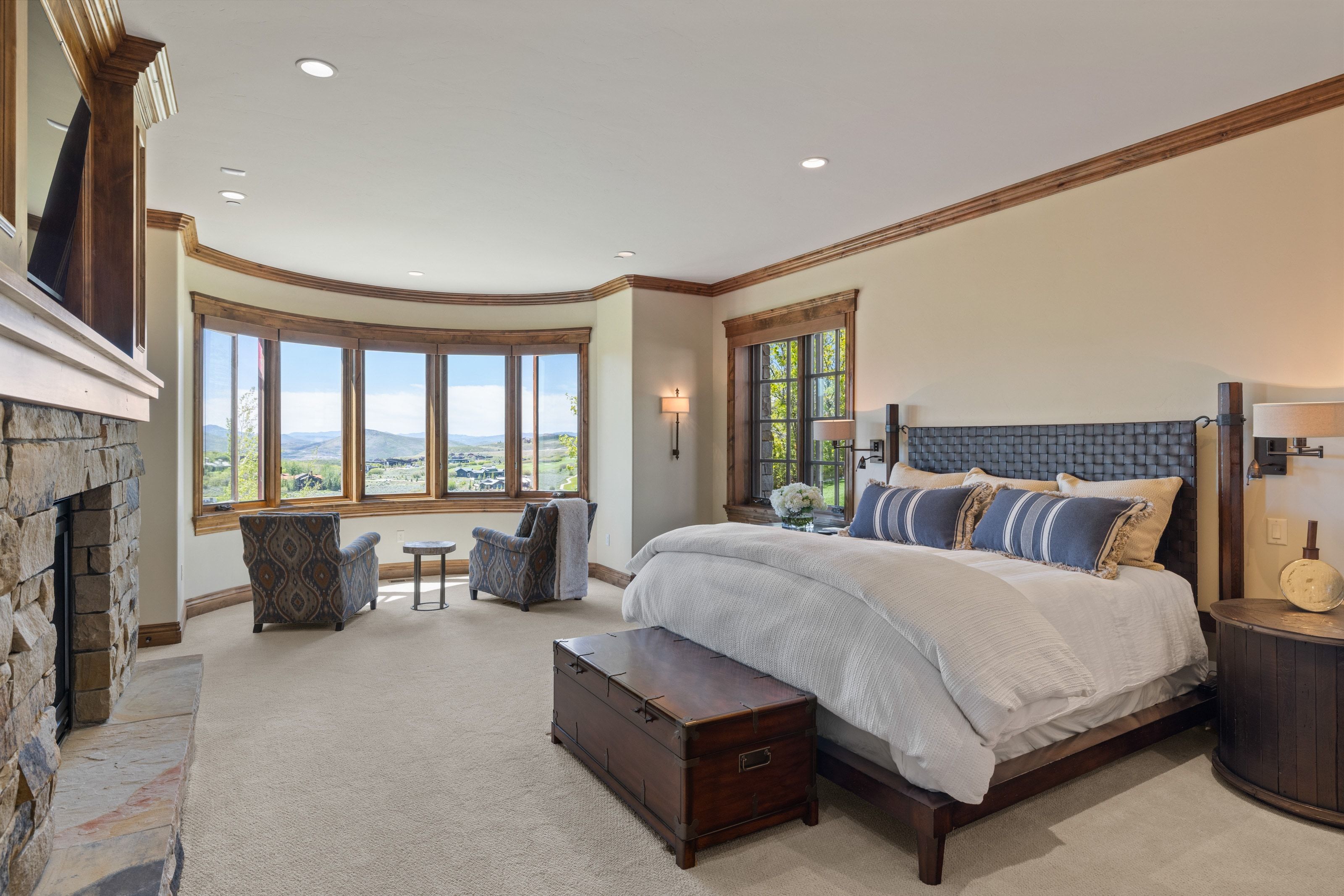Spacious room featuring a stone-clad fireplace, a curved bay window with wood-frame windows, recessed lighting, and crown molding