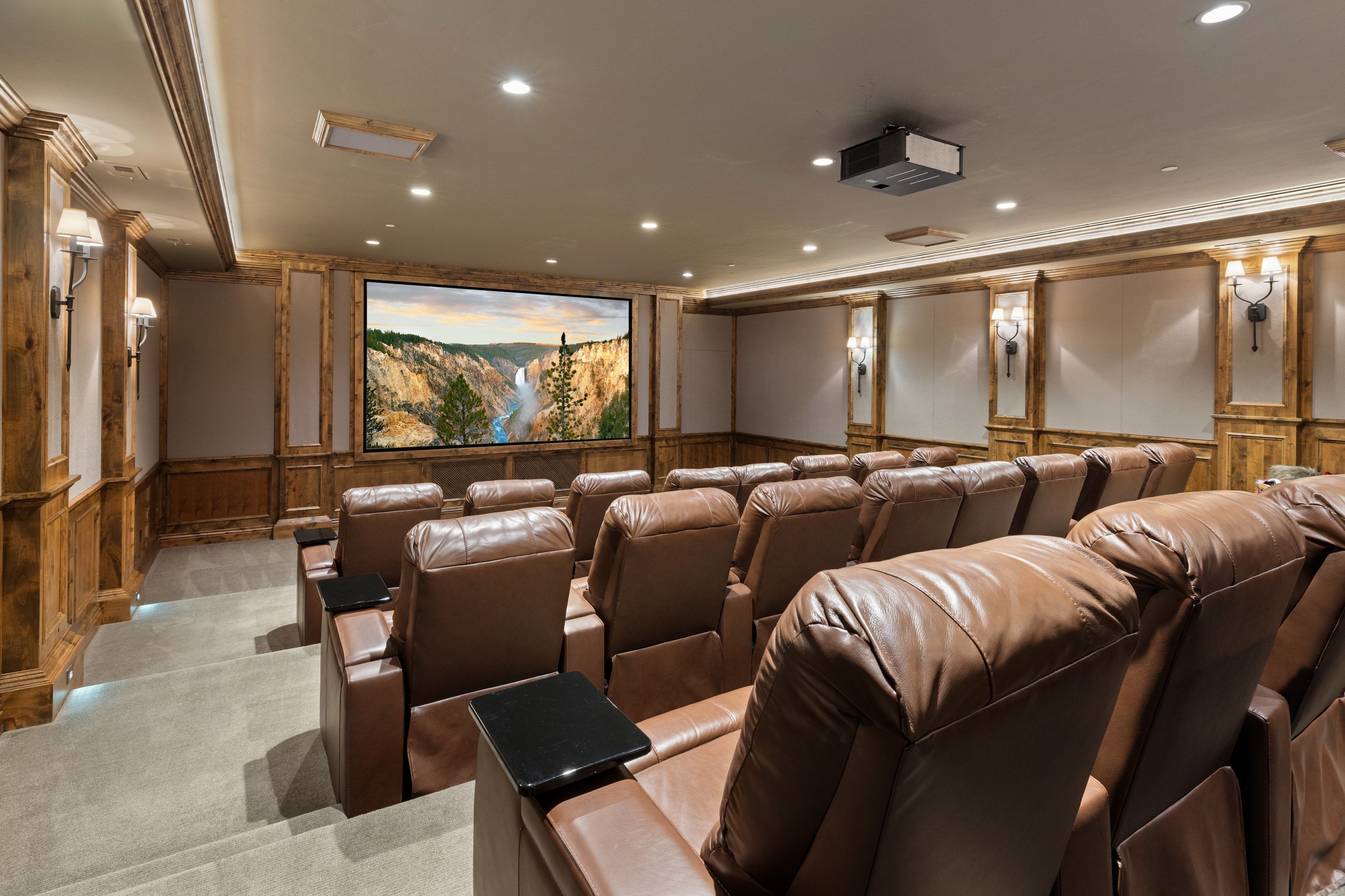 Dedicated home theater featuring tiered seating, a large projection screen, recessed lighting, wall sconces, and wood paneling with decorative trim