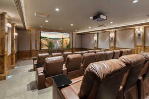 Dedicated home theater featuring tiered seating, a large projection screen, recessed lighting, wall sconces, and wood paneling with decorative trim