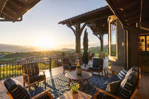Expansive outdoor deck featuring wood flooring, a dark metal railing, and a covered section with exposed timber beams