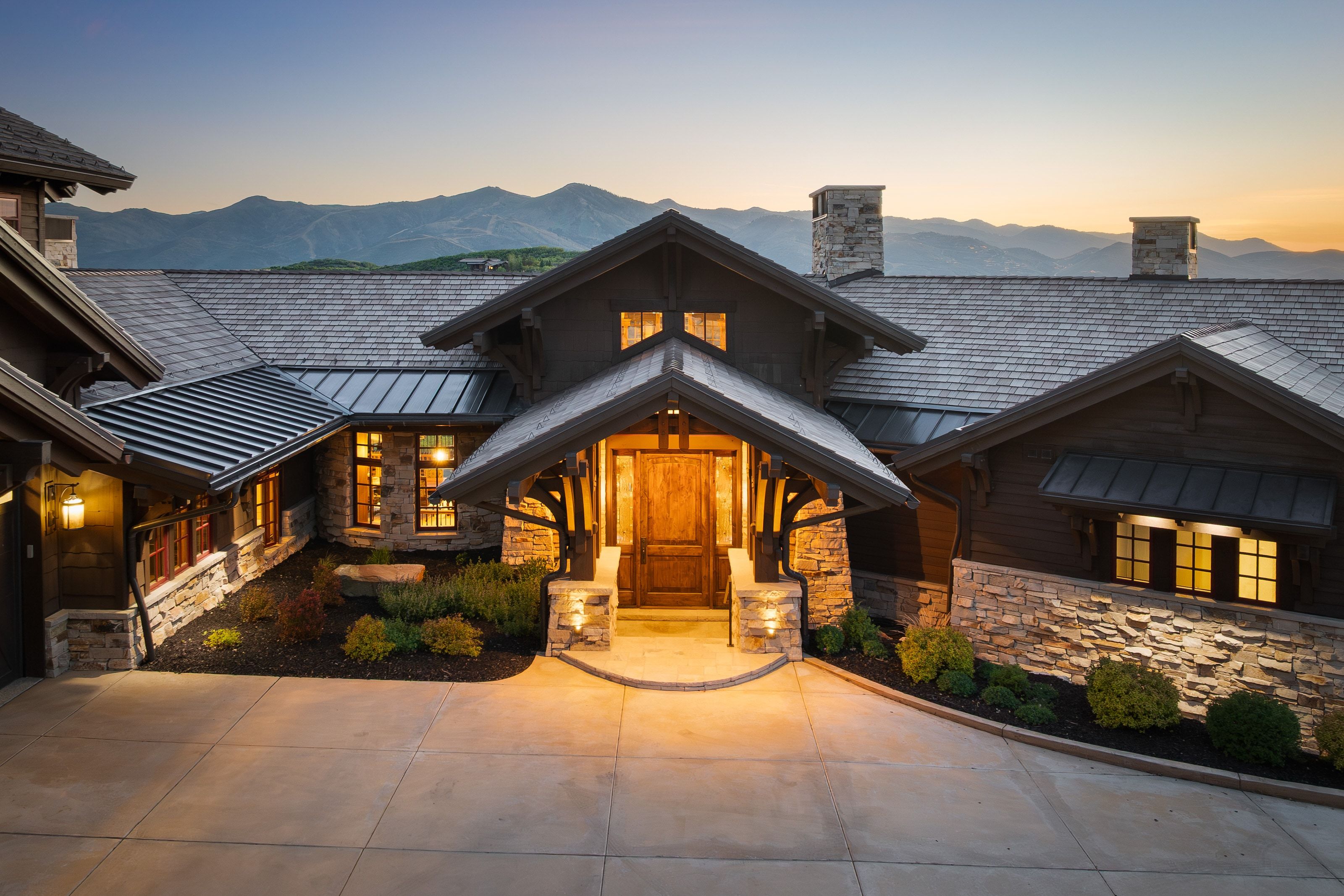 Craftsman-style exterior with stone and wood siding, prominent gabled entry with a solid wood door, concrete driveway, and mature landscaping