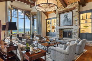 Great room featuring a stone fireplace with hearth seating, custom built-in cabinetry with integrated lighting, exposed wood ceiling beams, and a large arched window with mountain scenery