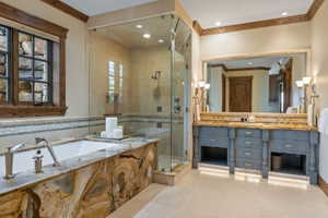 Spacious bathroom featuring a built-in bathtub with a striking natural stone surround, a separate glass-enclosed shower, a double vanity with undermount sinks, and integrated under-cabinet lighting