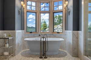 Freestanding tub with brass-finish fixtures, surrounded by marble wainscoting and a multi-pane bay window