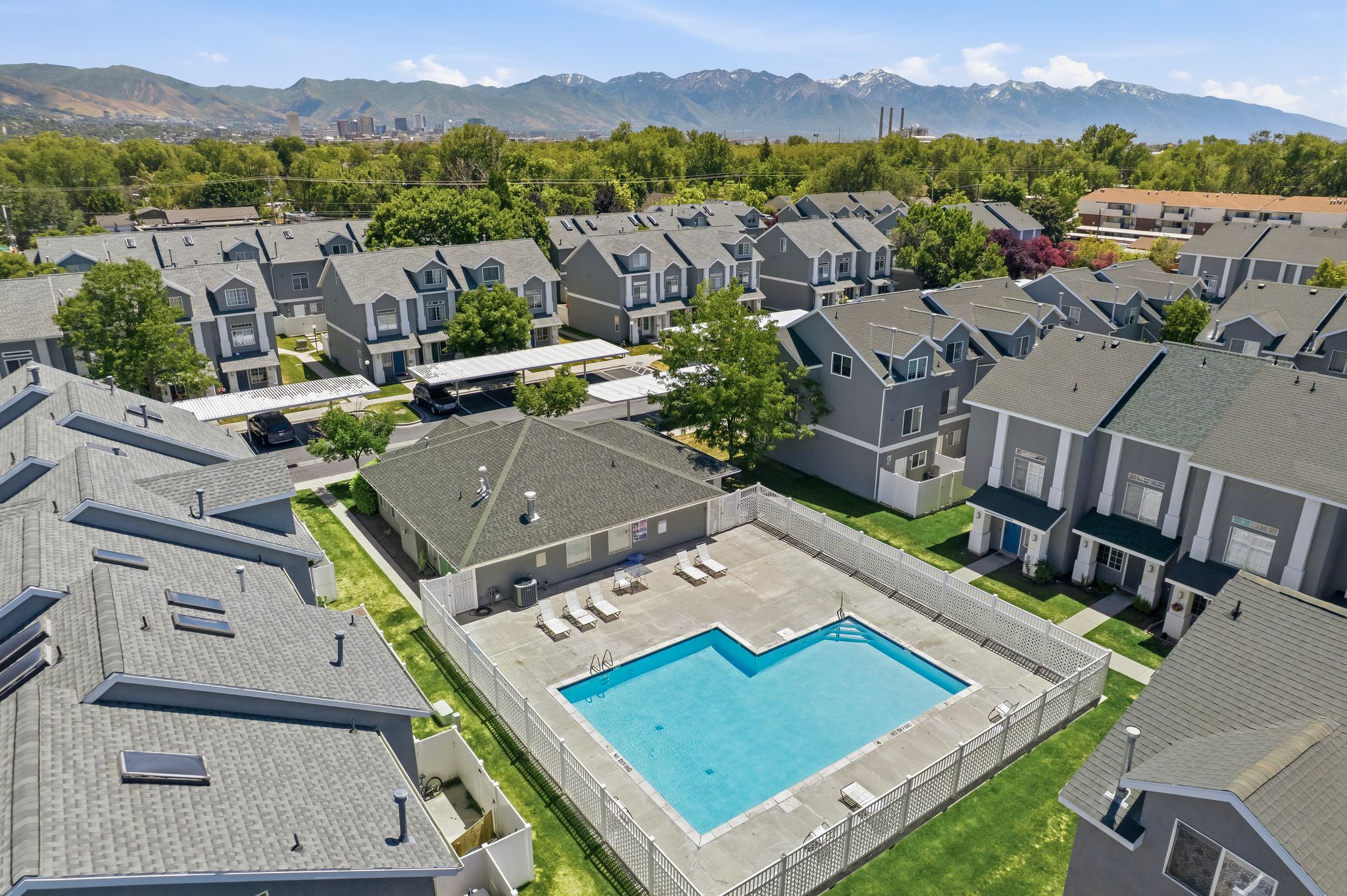 Community swimming pool with surrounding fence, adjacent to a building, with townhomes and covered parking structures in the background