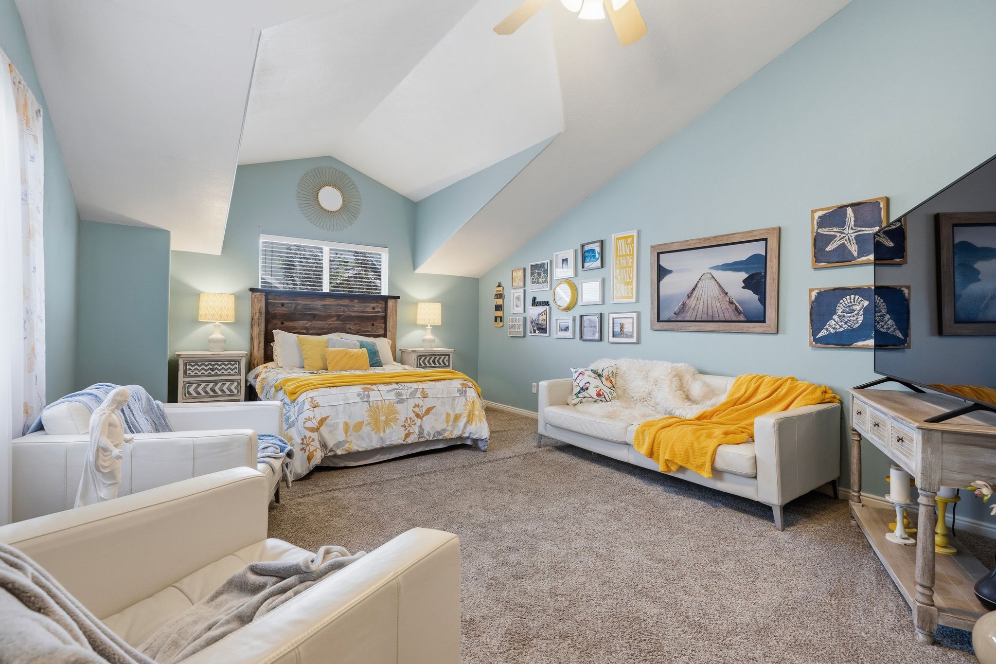 Spacious room featuring vaulted ceilings, a built-in ceiling fan, light blue walls, and a large window with blinds