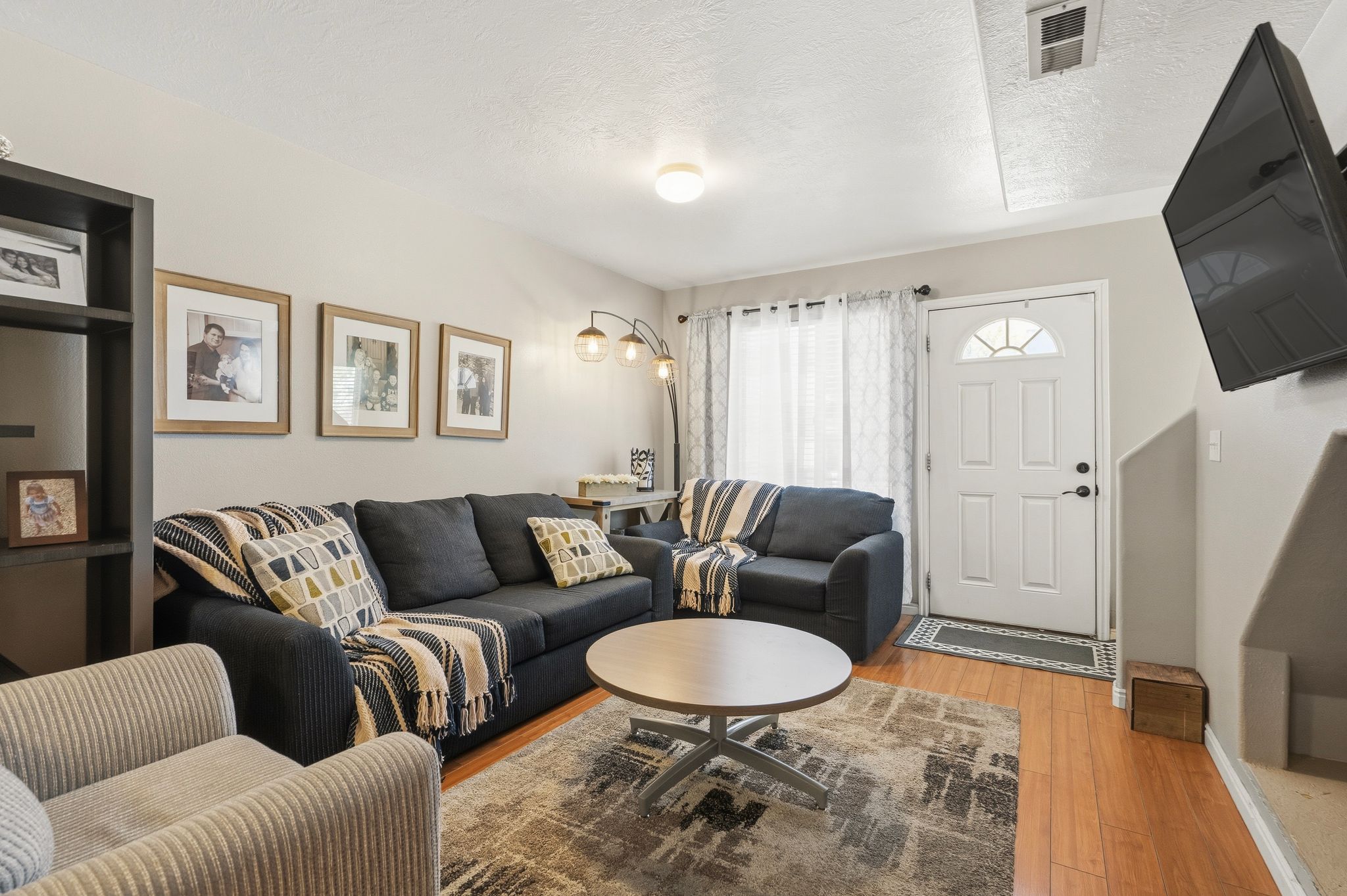 Living area featuring wood-finish flooring, a contemporary ceiling light fixture, a white entry door with an arched window, and a built-in shelving unit