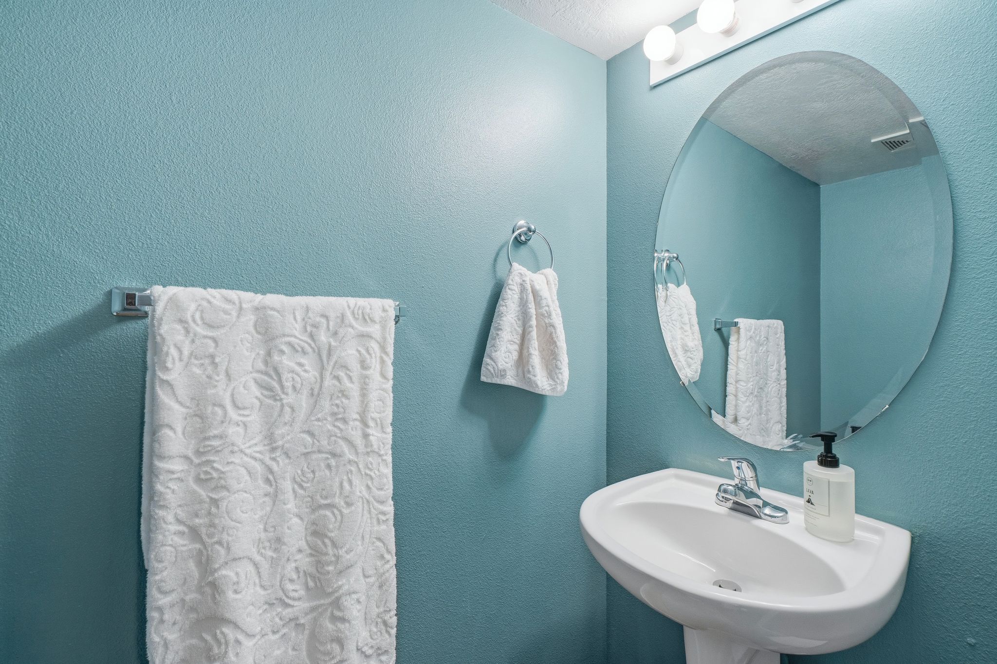 Pedestal sink with chrome faucet, complemented by a large oval mirror