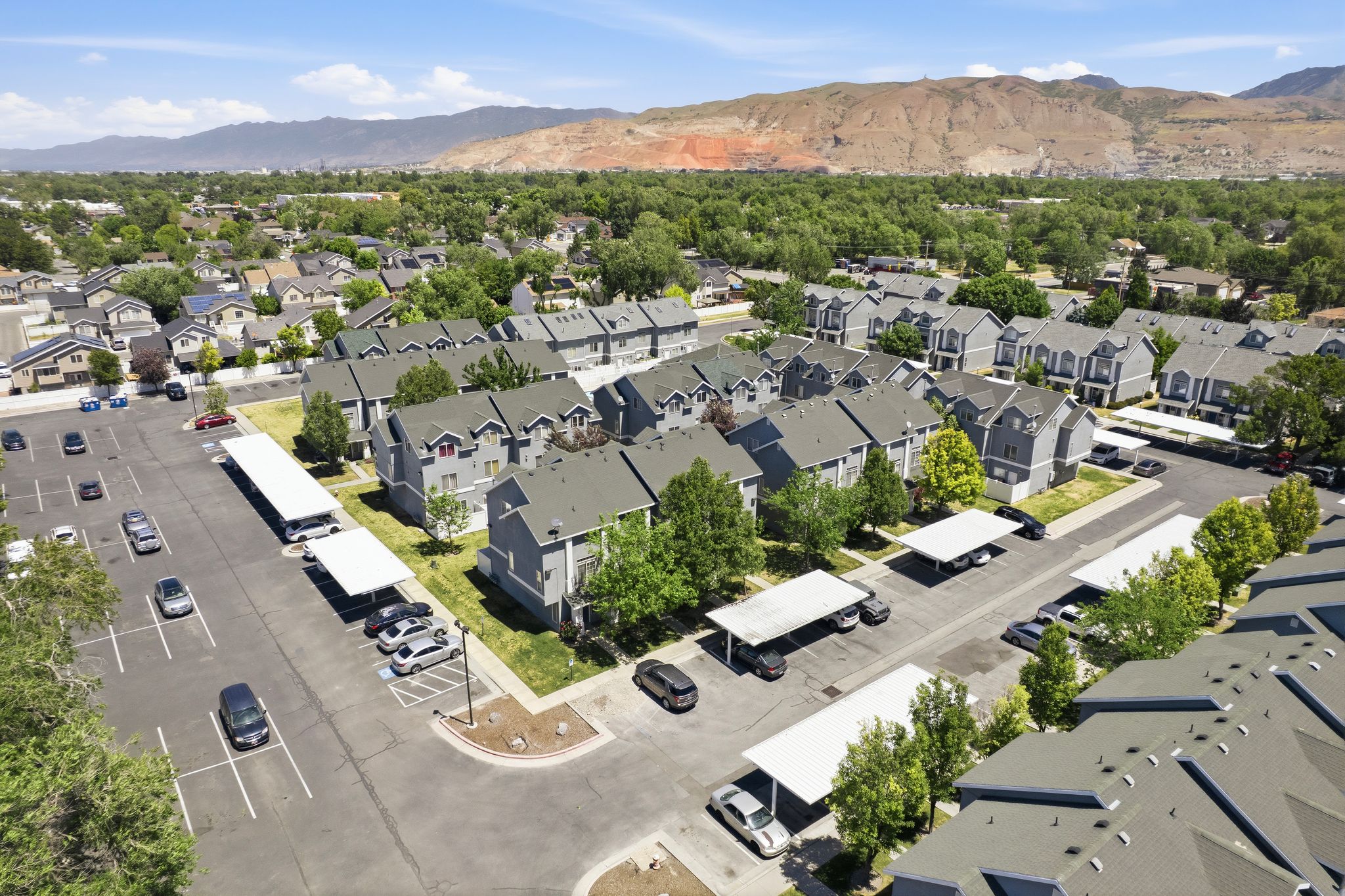 Multi-building property featuring covered parking structures, mature landscaping, and a distant mountain backdrop