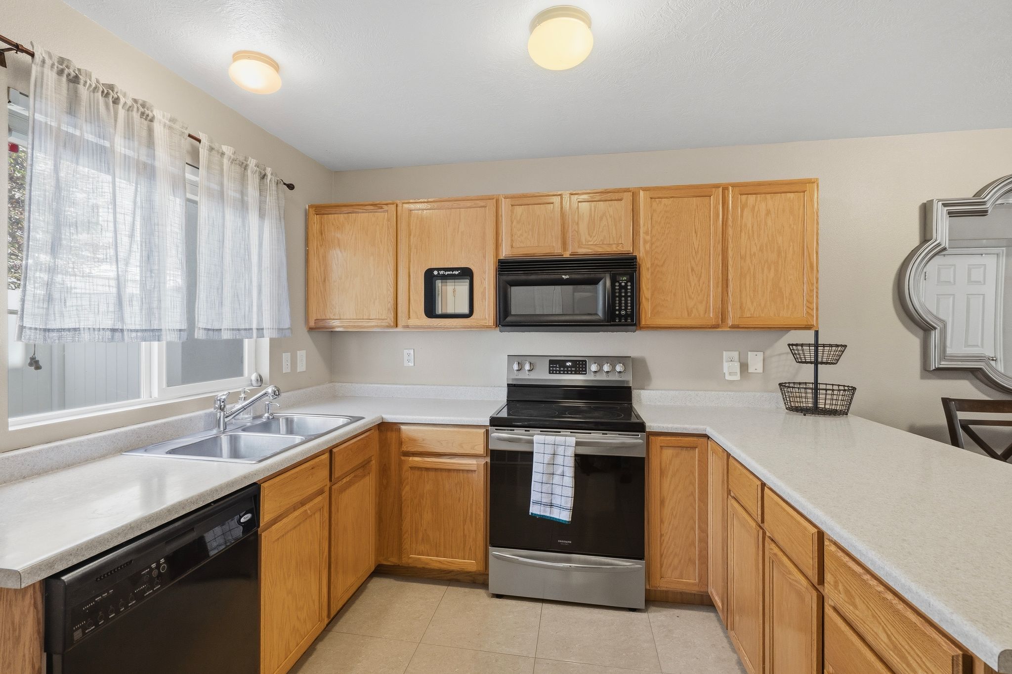 Kitchen featuring wood cabinetry, light-toned countertops, a double basin stainless steel sink, and a window above the sink