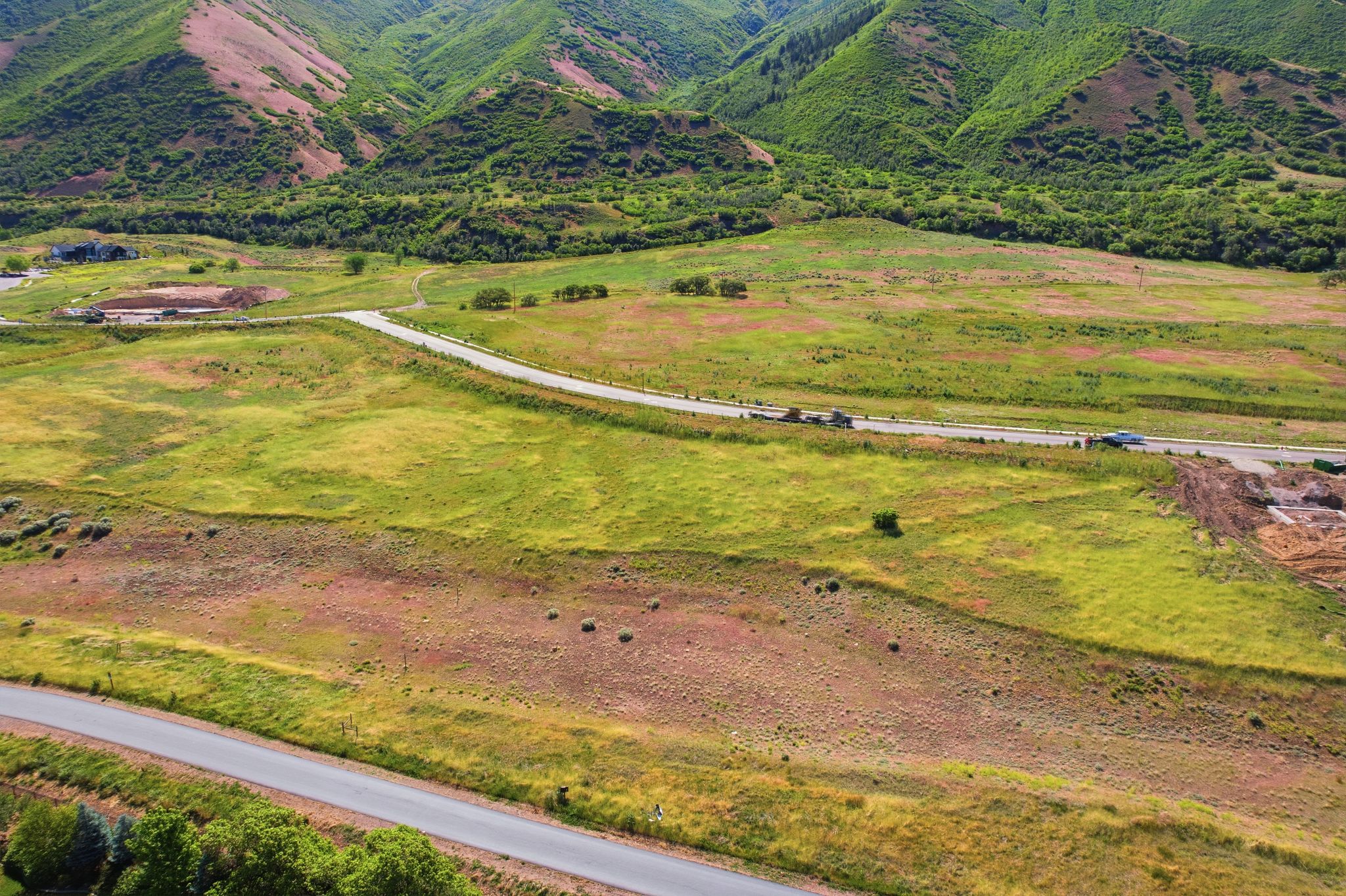 Expansive undeveloped land featuring a paved road, natural green and brown vegetation, and mountainous terrain in the background