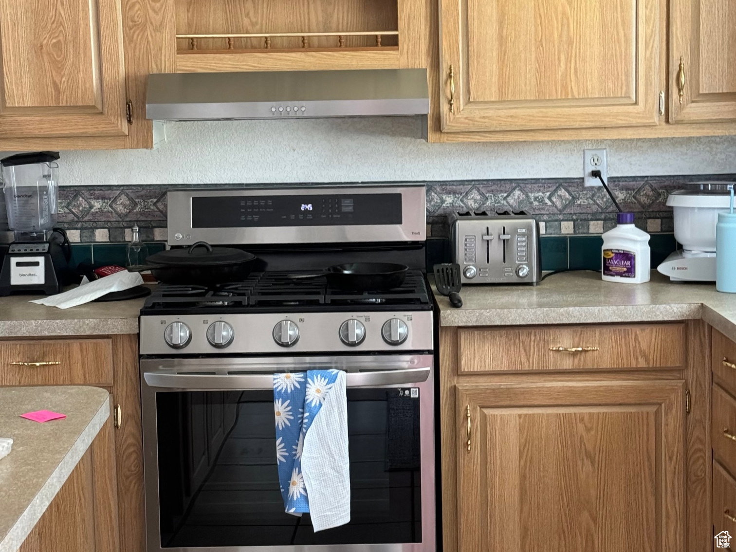 Stainless steel range with matching range hood, light wood-finish cabinetry, and laminate countertops