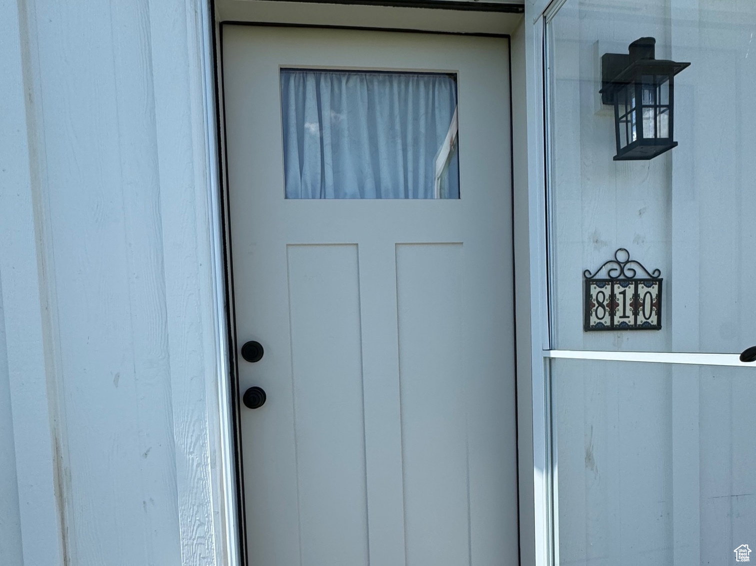 Front entrance featuring a white panel door with a window, matte black hardware, and a glass storm door