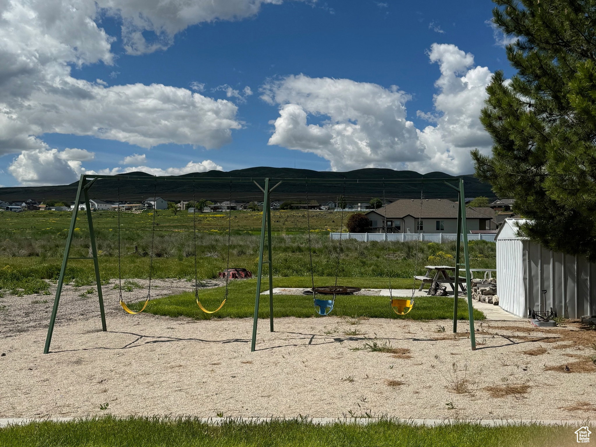 Expansive outdoor space featuring a swing set with sand bedding, a built-in fire pit, and a picnic table on a concrete patio
