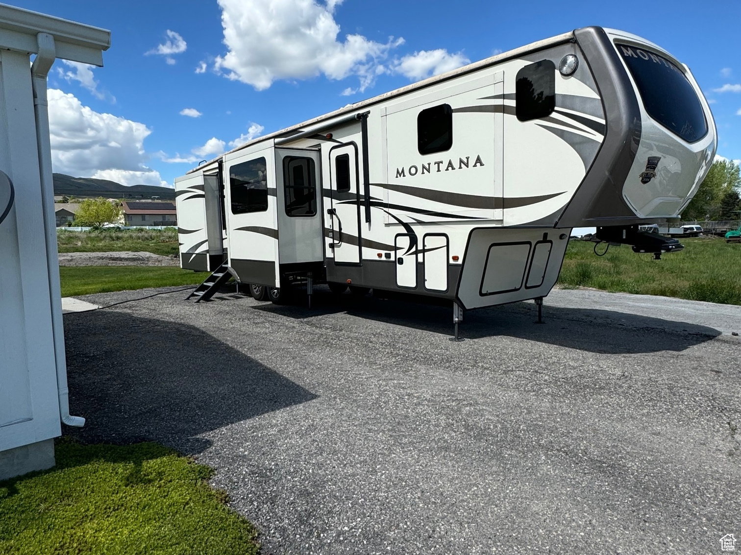 Modern fifth-wheel recreational vehicle with a white and gray exterior, multiple slide-outs, integrated entry steps, and a large front window