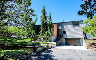 Contemporary multi-level residence featuring light gray siding, a prominent brick accent wall, and a modern garage door with frosted glass panels