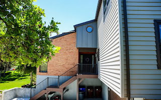 Multi-level exterior featuring brick and horizontal siding, a prominent wood staircase with black metal railings, a circular window, and a covered entry