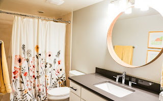 Bathroom featuring a vanity with an undermount sink and a dark countertop, an overhead lighting fixture, and a wall-mounted round mirror