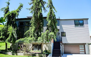 Split-level residence featuring a wood-panel garage door, gray siding, and an exterior staircase