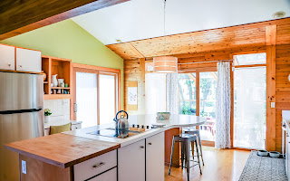 Kitchen featuring a central island with integrated cooktop, light wood cabinetry, stainless steel refrigerator, wood-finish flooring, and a vaulted ceiling with exposed wood beams