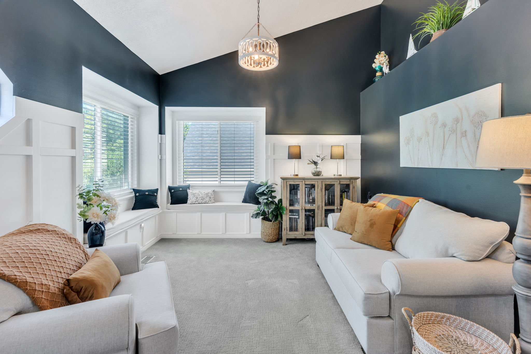 Vaulted ceiling living area featuring a built-in window bench, white wainscoting, and carpet flooring