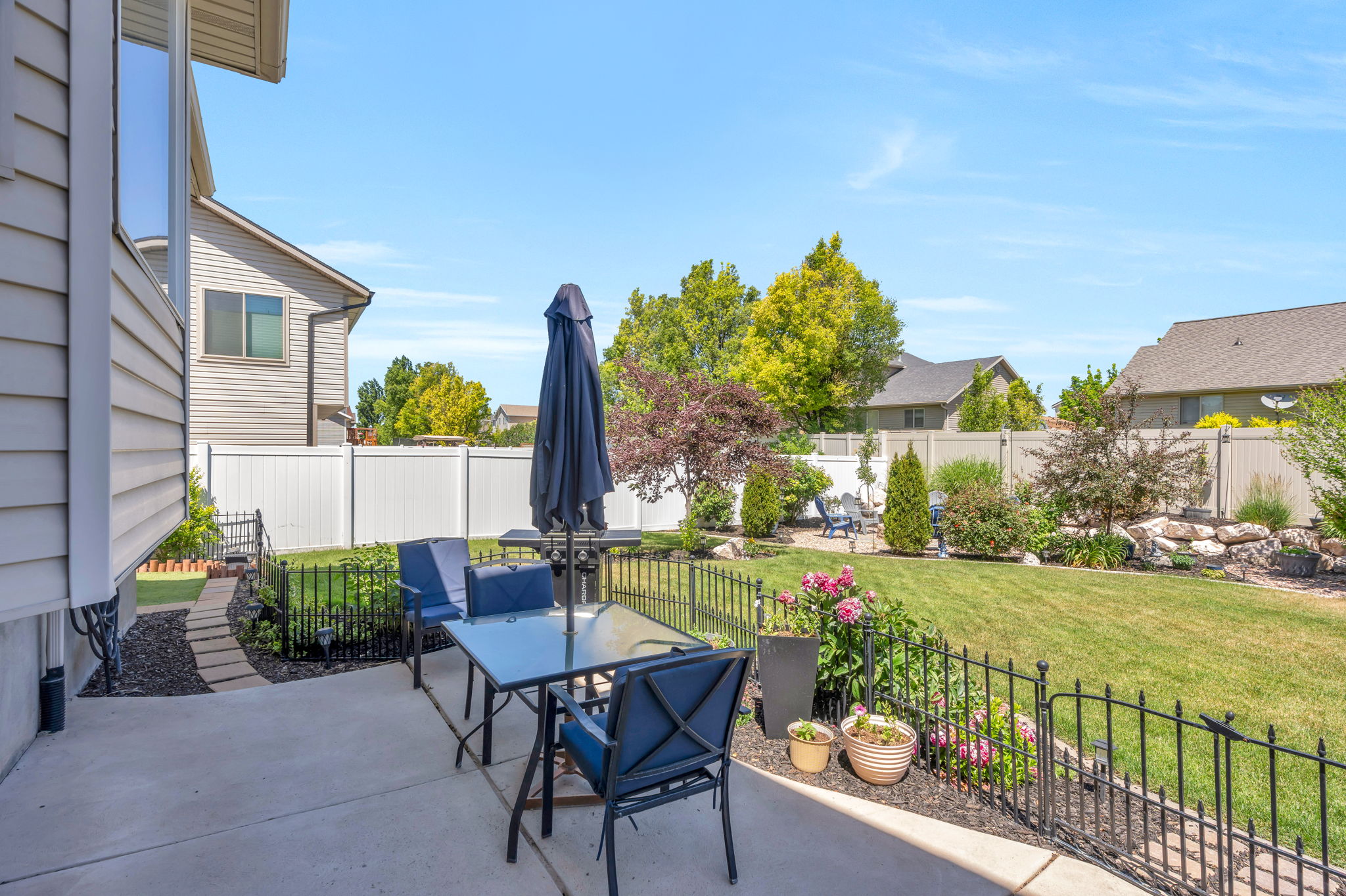 Concrete patio featuring a glass-top table, a black metal fence, and a stepping stone path leading to a spacious lawn