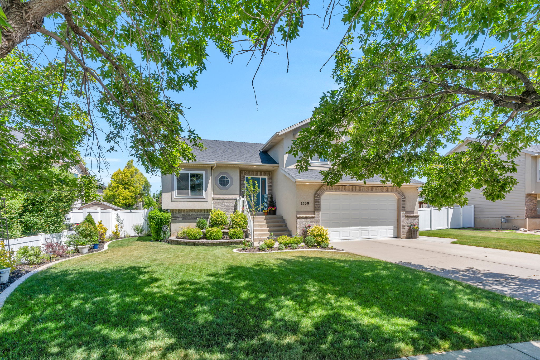 Split-level residence featuring a two-car garage, manicured lawn, and mature trees providing natural shade