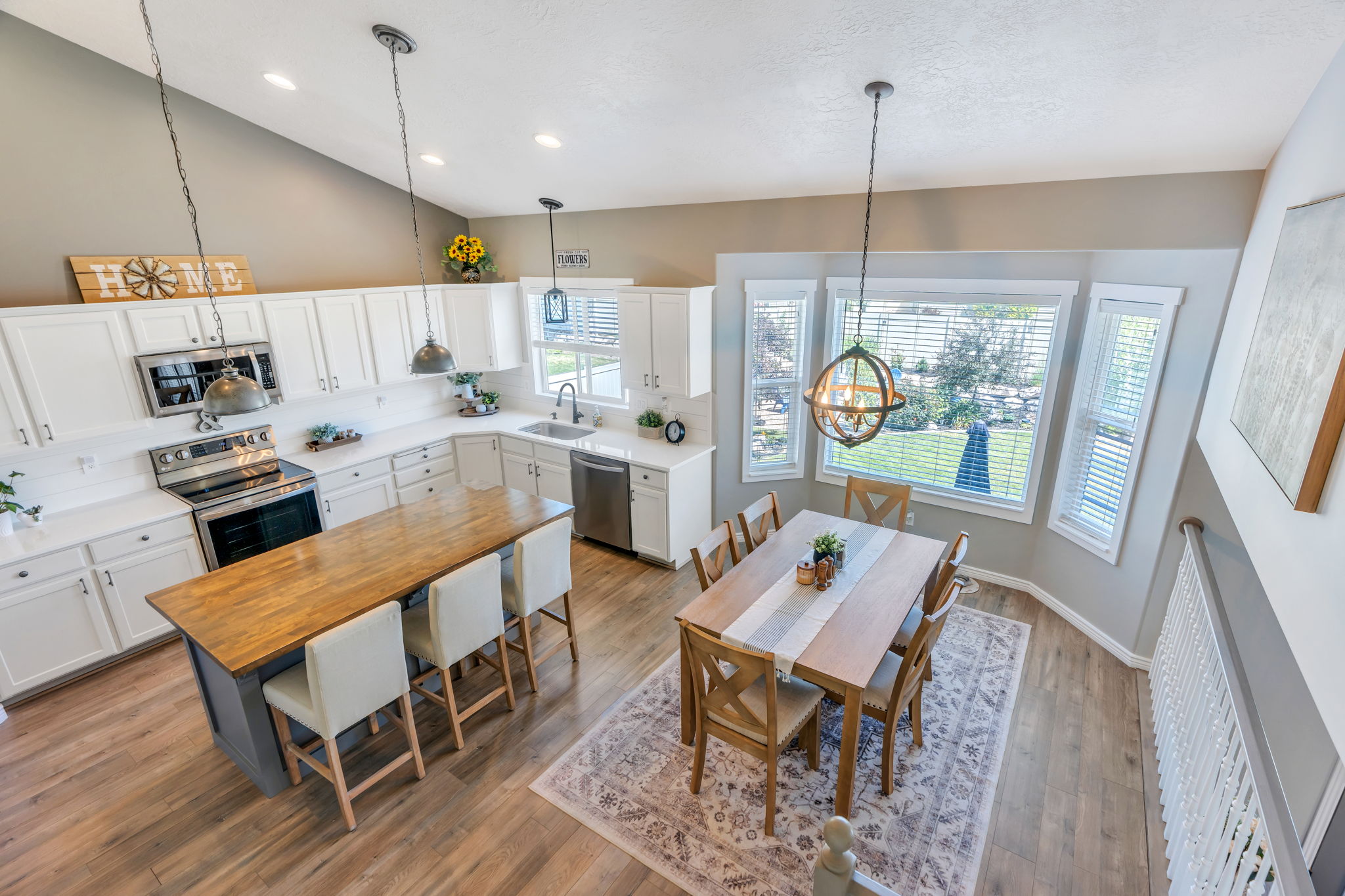 Vaulted ceiling kitchen featuring white cabinetry, stainless steel appliances, a wood-finish island with seating, and wood-finish flooring