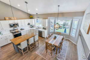 Vaulted ceiling kitchen featuring white cabinetry, stainless steel appliances, a wood-finish island with seating, and wood-finish flooring