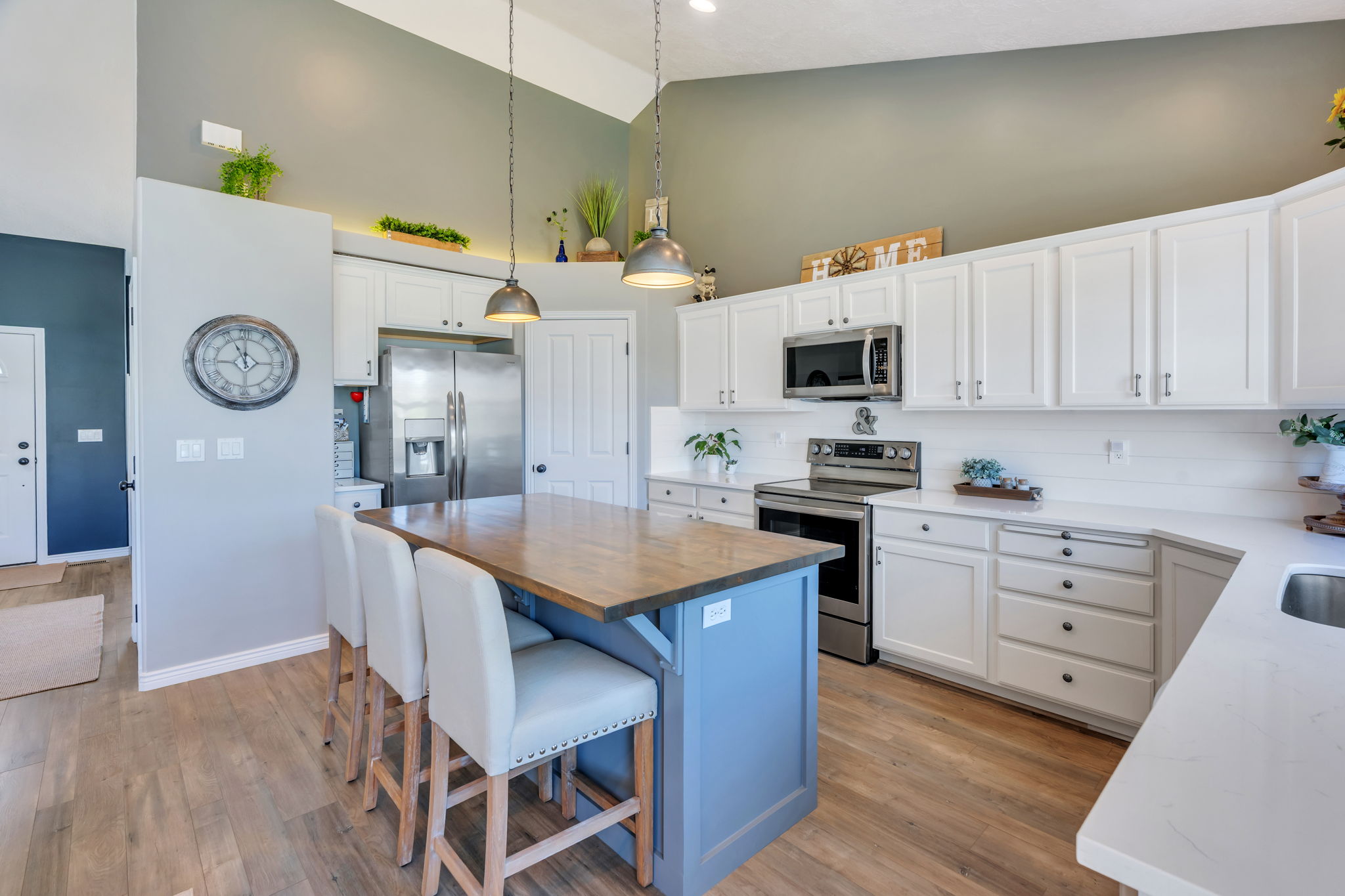Kitchen featuring a central island with a wood-finish countertop and blue base, white cabinetry with silver hardware, stainless steel appliances, and light wood-finish flooring