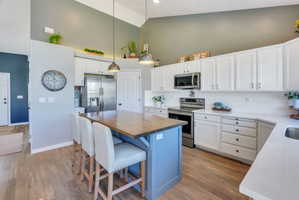 Kitchen featuring a central island with a wood-finish countertop and blue base, white cabinetry with silver hardware, stainless steel appliances, and light wood-finish flooring