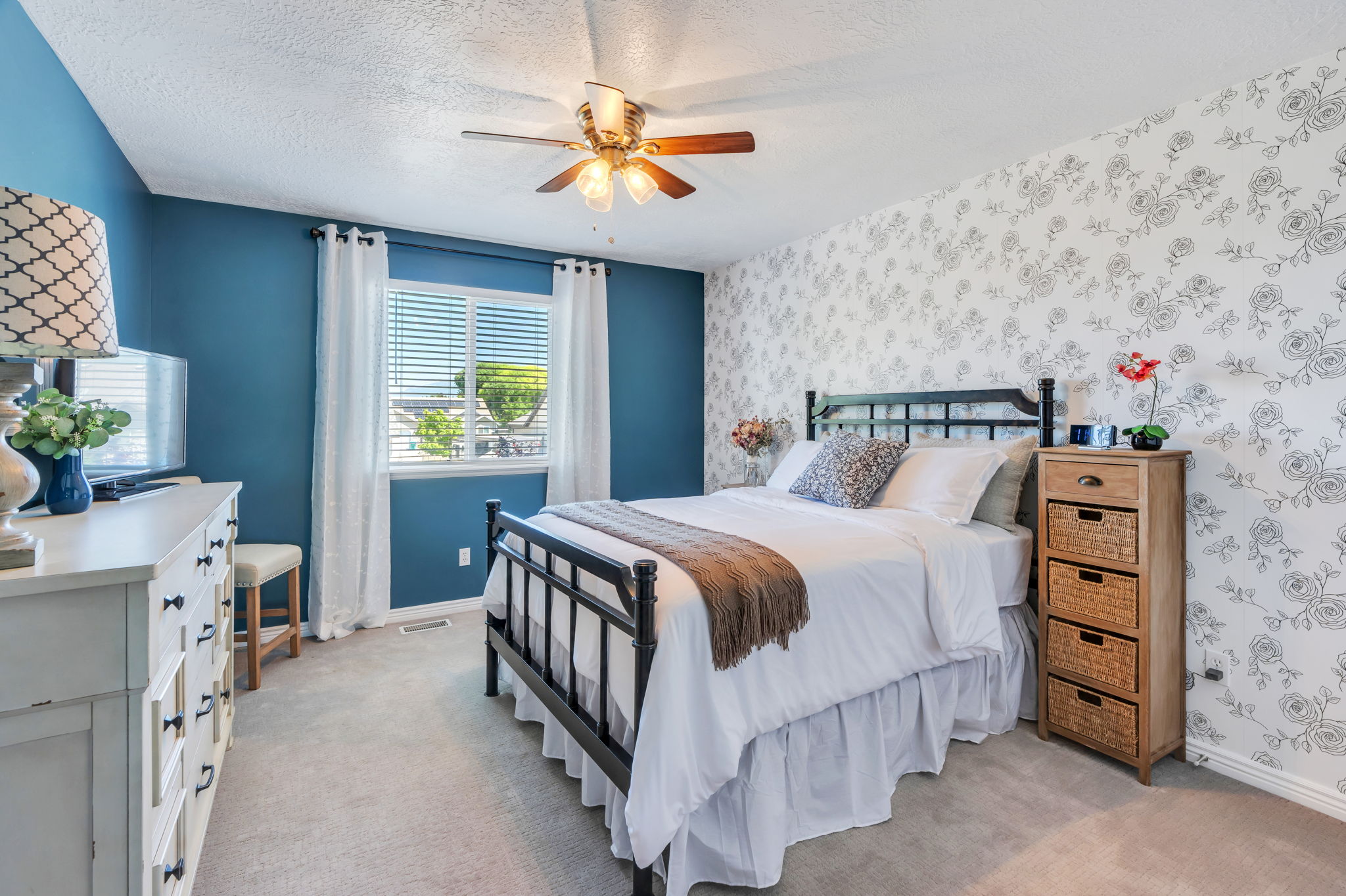 Bedroom featuring a ceiling fan with integrated lighting, a window with blinds and white curtains, and carpet flooring