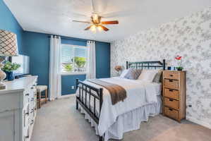 Bedroom featuring a ceiling fan with integrated lighting, a window with blinds and white curtains, and carpet flooring