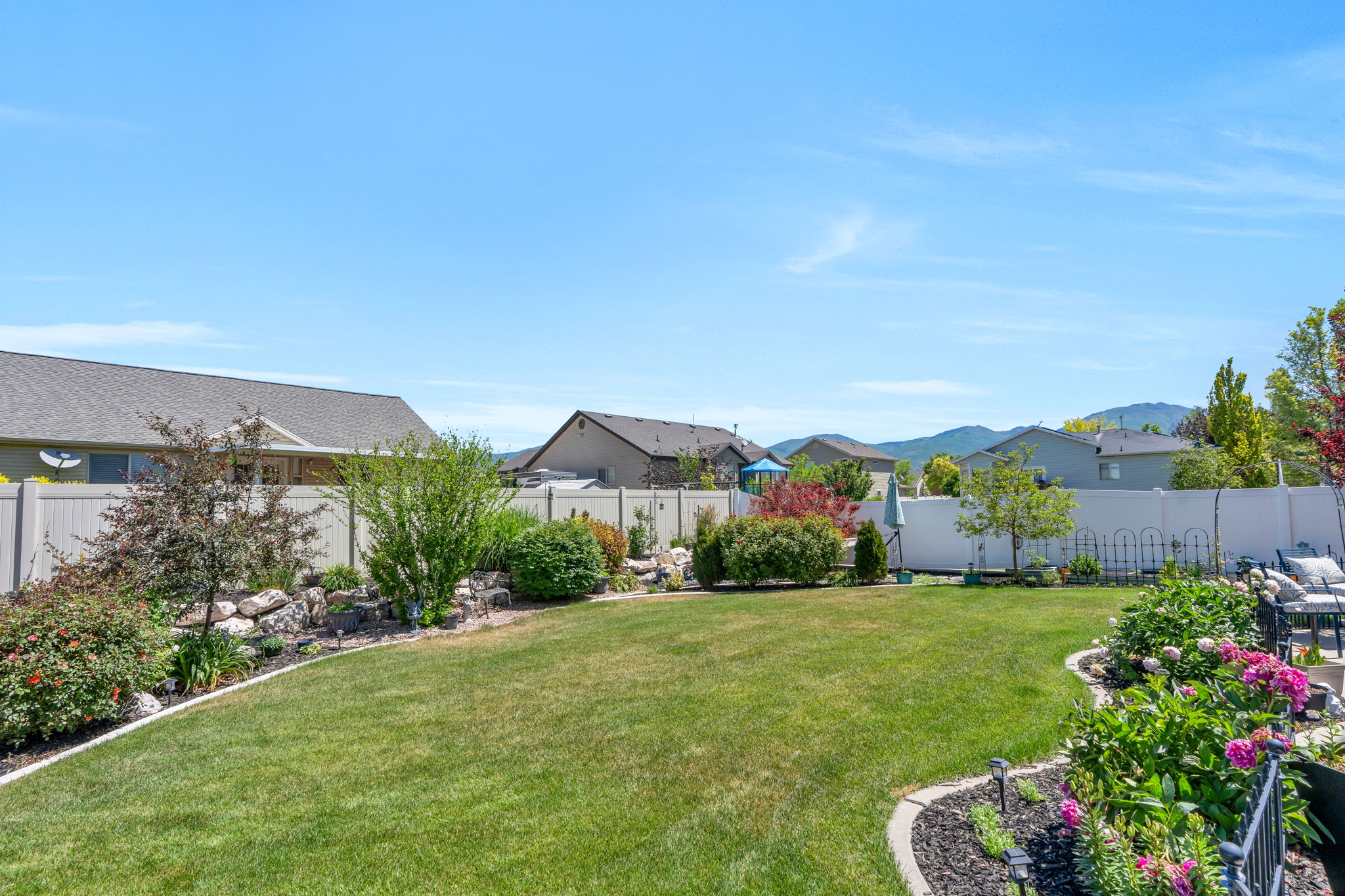 Spacious backyard featuring a manicured lawn, established landscaping beds, and a white privacy fence