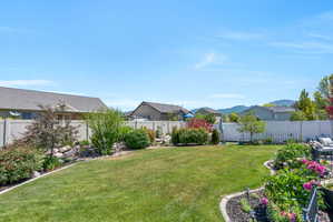 Spacious backyard featuring a manicured lawn, established landscaping beds, and a white privacy fence