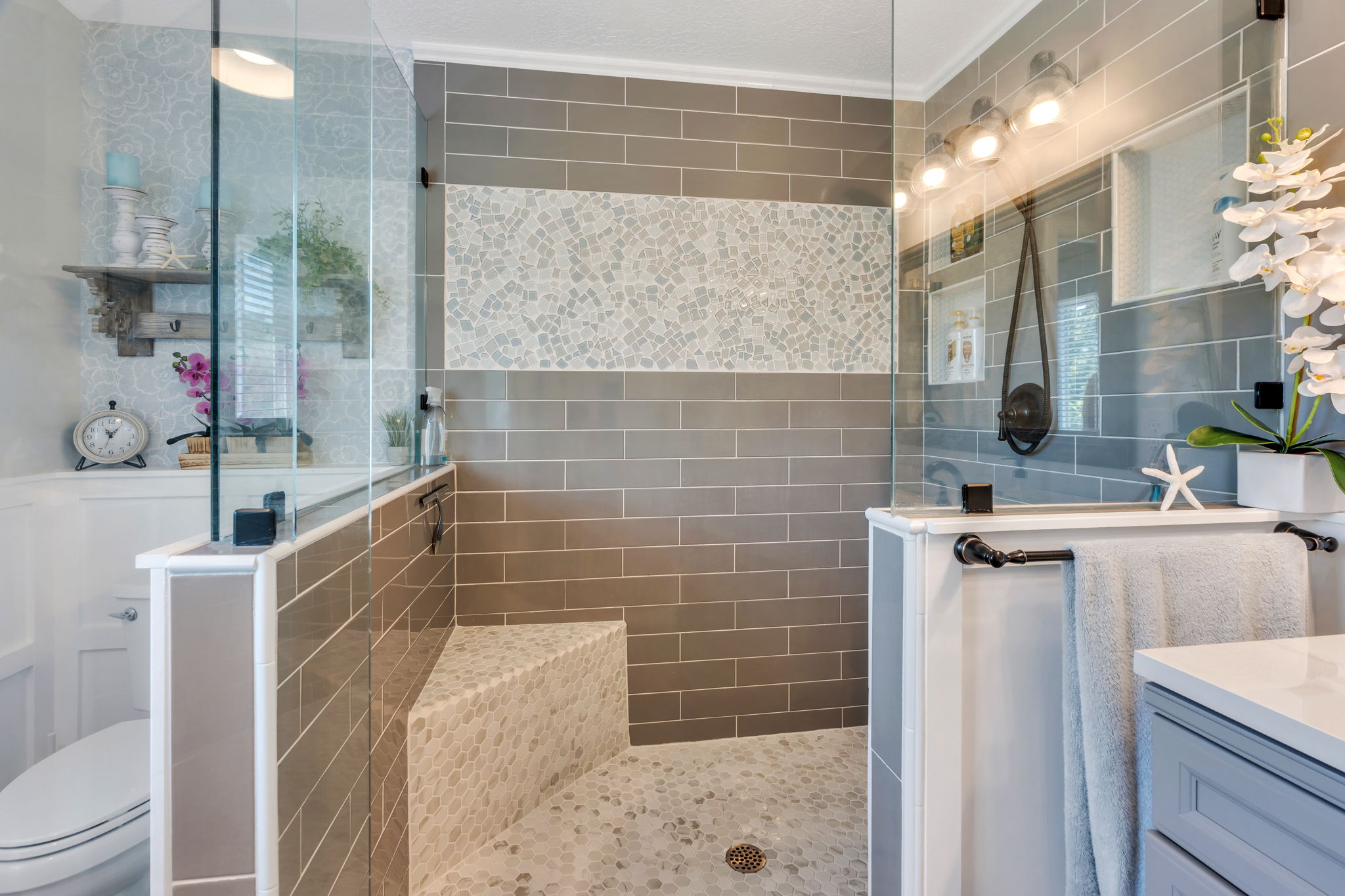 Walk-in shower featuring glass enclosure, subway tile walls, pebble tile flooring, and an integrated pebble tile bench