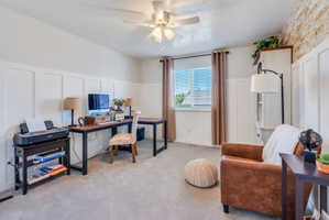 Board and batten wainscoting frames this versatile room, featuring a window with blinds, ceiling fan, and neutral carpet flooring