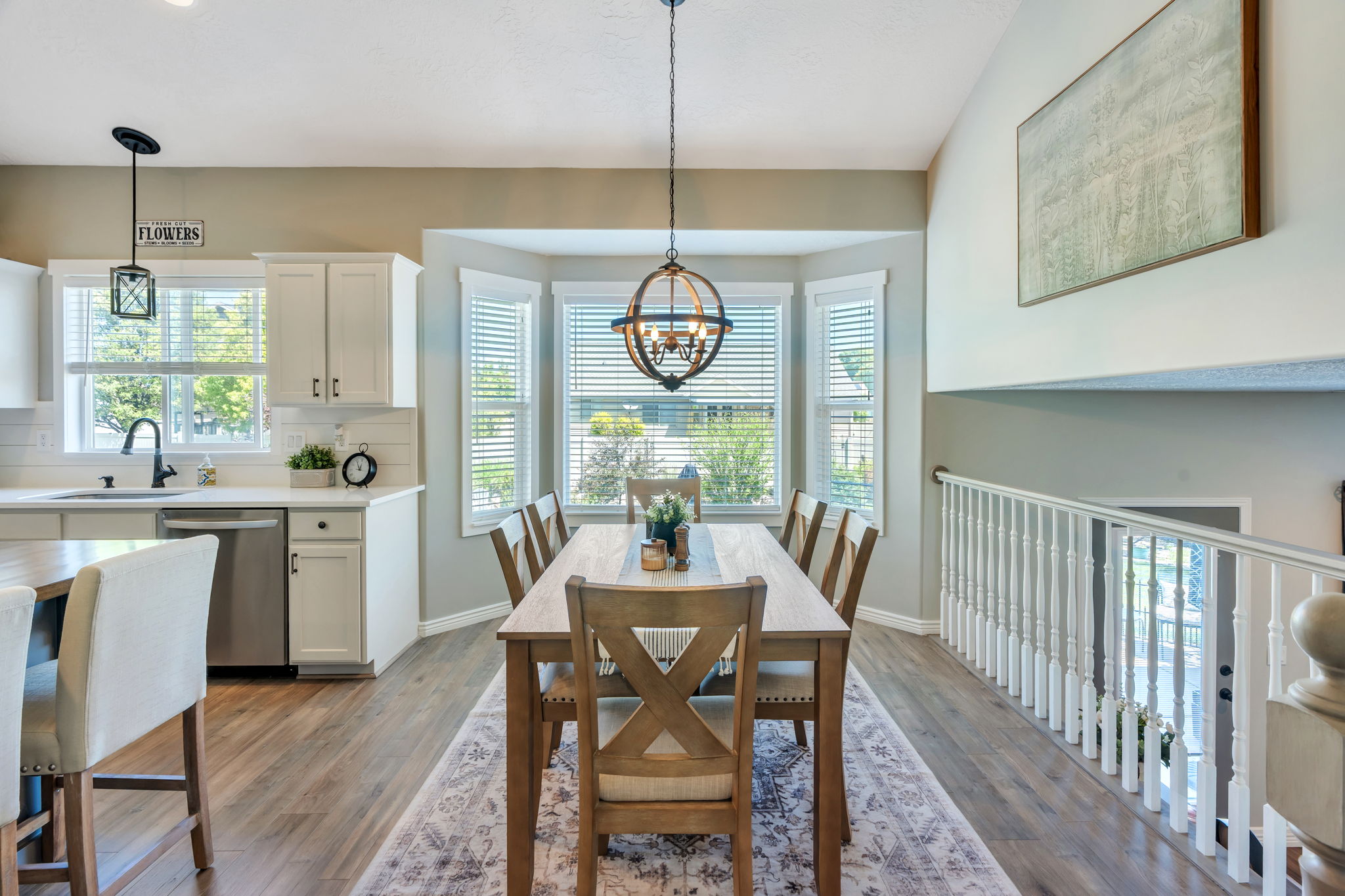 Open-concept dining area with wood-finish flooring, a bay window, and an overhead chandelier
