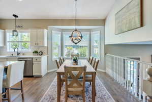 Open-concept dining area with wood-finish flooring, a bay window, and an overhead chandelier