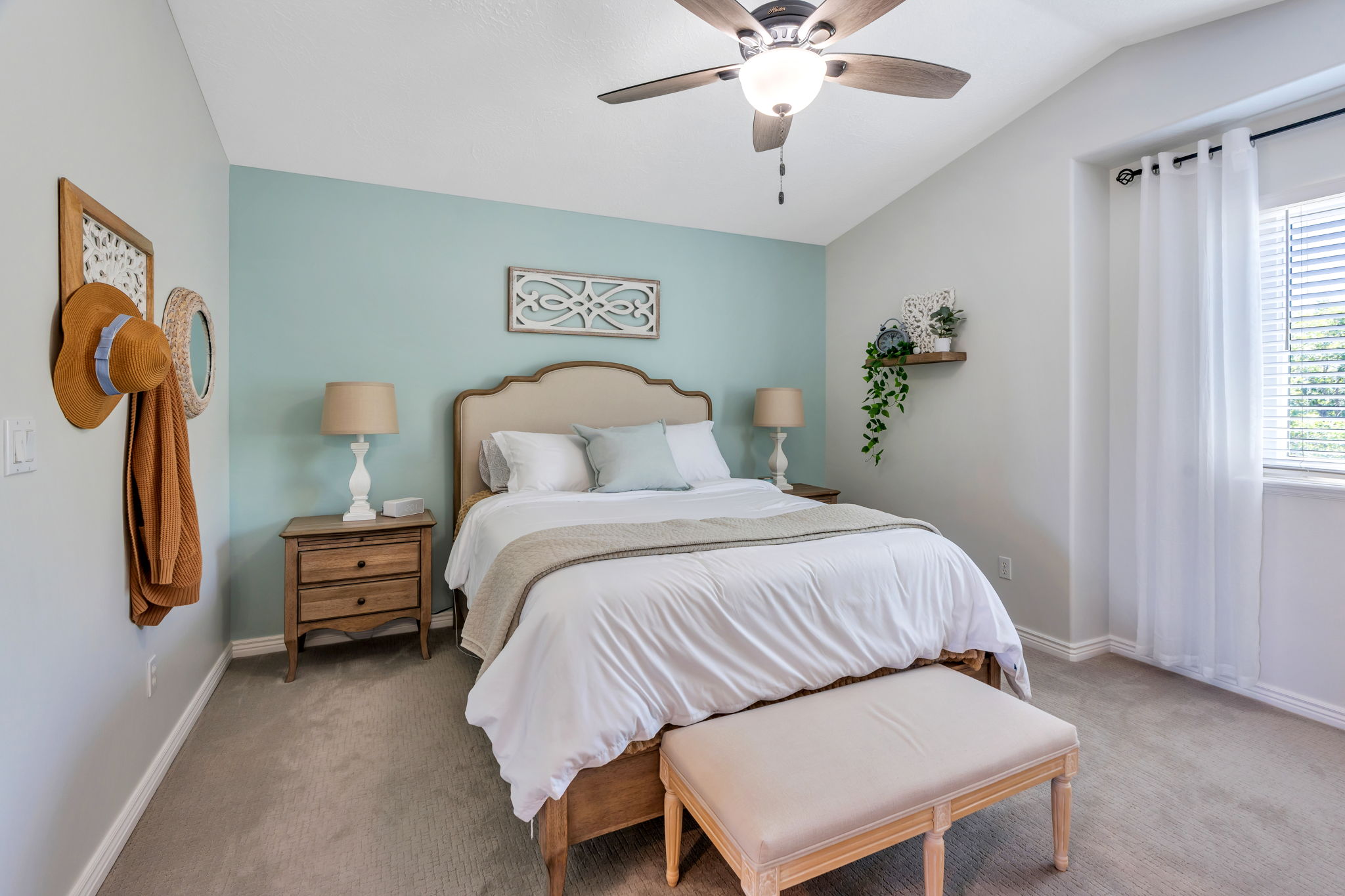 Bedroom featuring an upholstered headboard, wood-finish nightstands, a ceiling fan with integrated lighting, a window with blinds, and light-colored carpeting