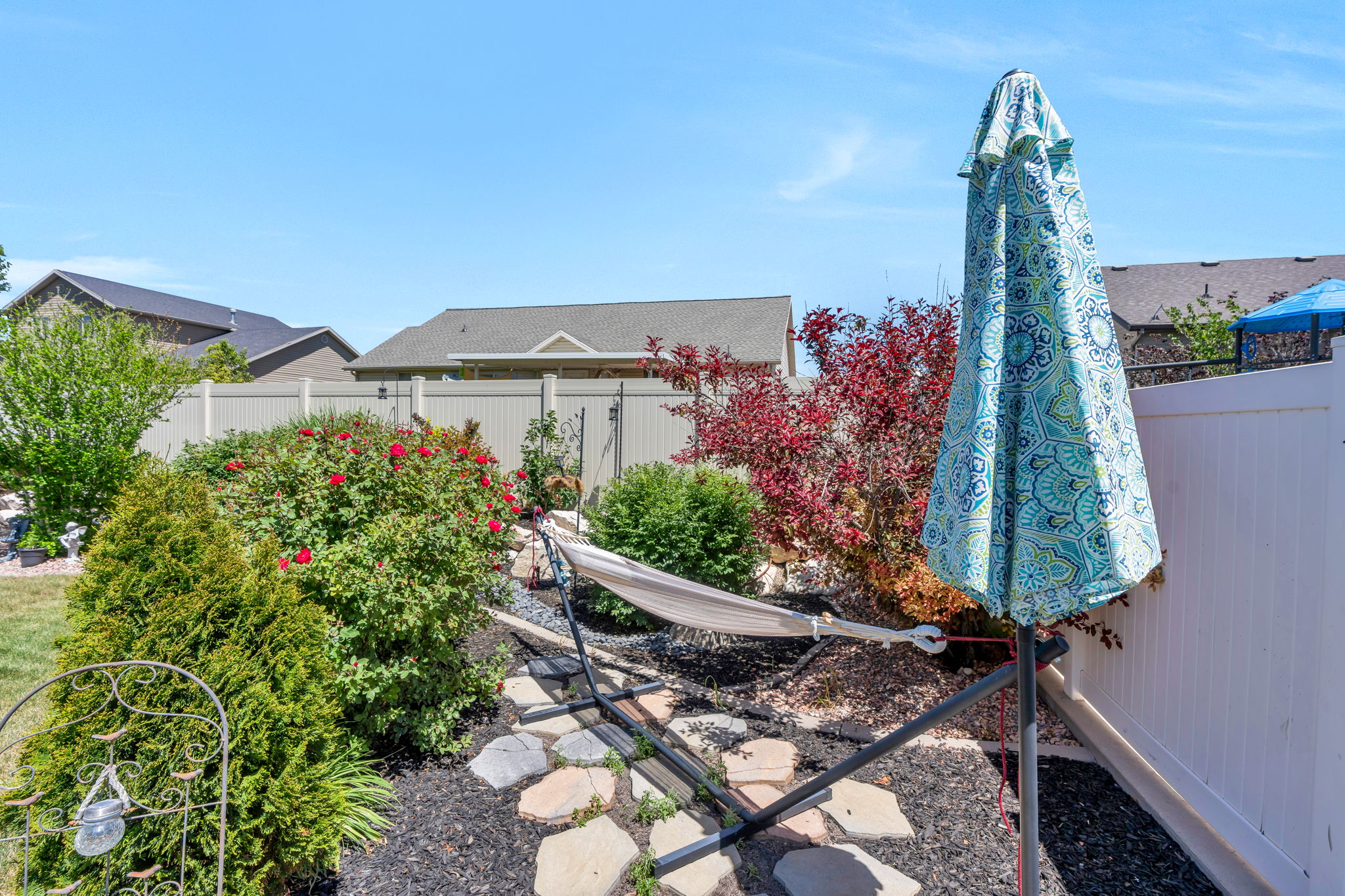 Landscaped backyard featuring established shrubs, flowering bushes, a stone pathway, and a privacy fence