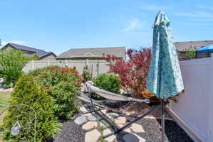 Landscaped backyard featuring established shrubs, flowering bushes, a stone pathway, and a privacy fence
