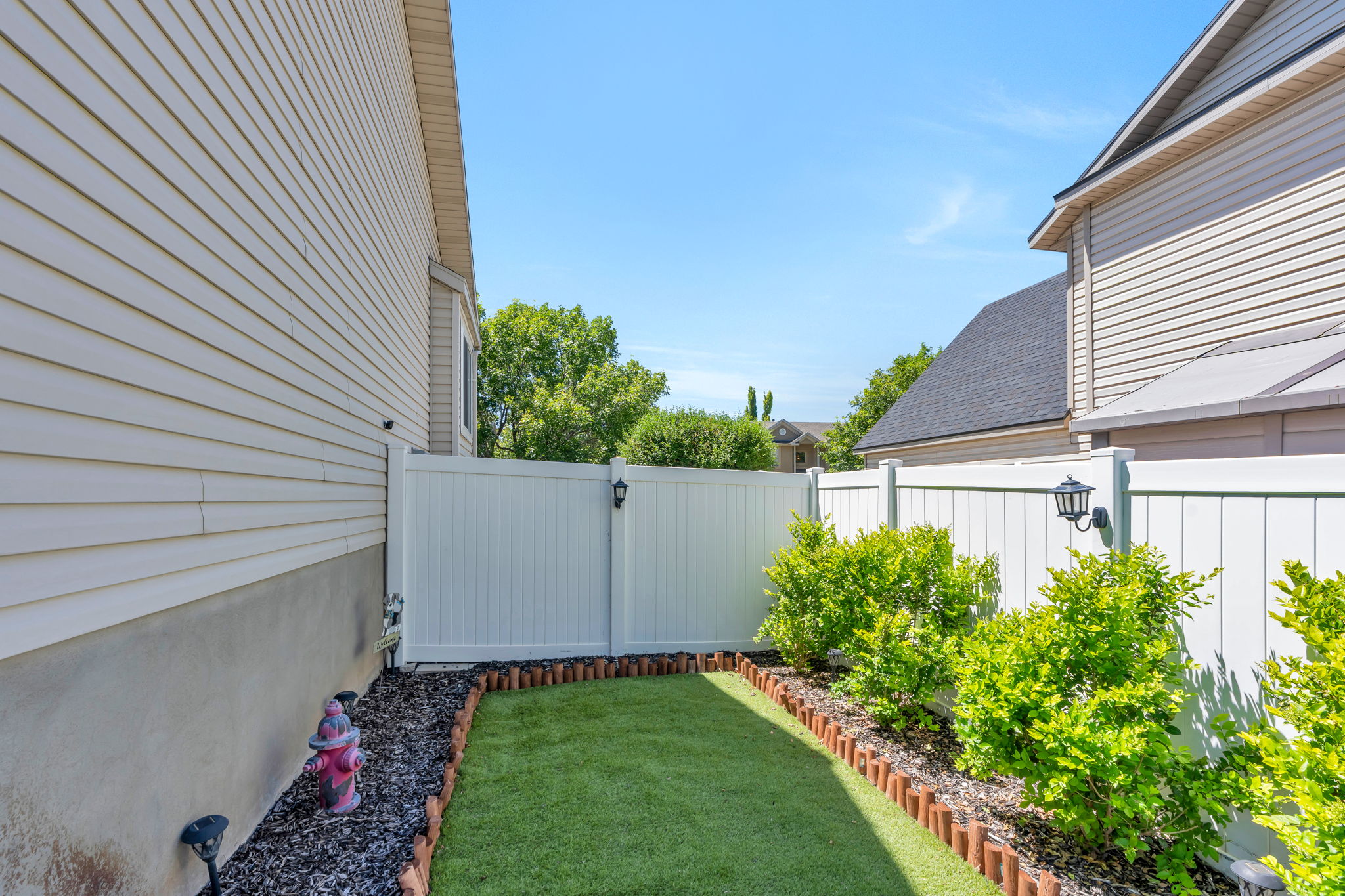 Private side yard featuring artificial turf and defined planting beds with mature shrubs